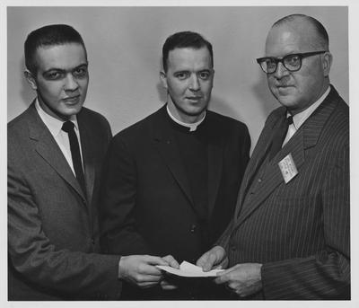 Religion in Life Week; An unidentified man (right), an unidentified priest (center) and Dr. Young are holding a piece of paper during the Religion in Life Week