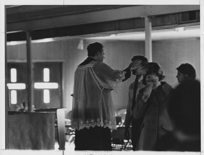 A priest putting ashes on unidentified students' foreheads on Ash Wednesday in the Newman Center; This is in the 1969 Kentuckian on page 126, picture number 1