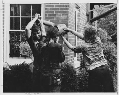 Delta Delta Delta sisters plus a male friend play around with a bucket of water in front of the sorority house; This image is in the 1969 Kentuckian on page 310, image 1