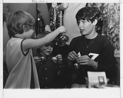 Delta Zeta sister decorating a Christmas tree with children; This image is in the 1969 Kentuckian on page 314, image 1