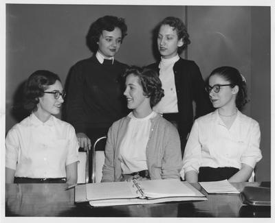 Female students standing and sitting at a table; Elizabeth Kentley stands, left
