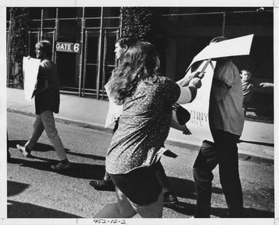 Woman hits man on head with a poster during a protest; This image is in the 1969 Kentuckian on page 12, image 2