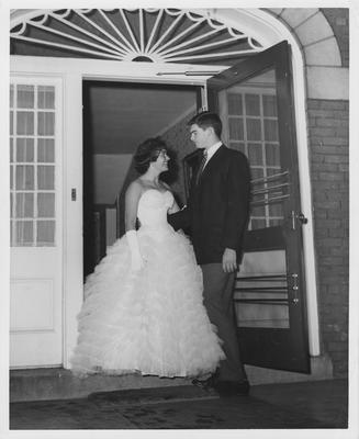 Sorority woman in formal dress stands with her date in a doorway; This photo is in the 1957 Kentuckian on page 7