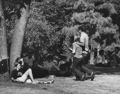 Students rest and relax under trees on the University of Kentucky campus in between classes; This photo is in the 1969 Kentuckian on page 131, image number 1