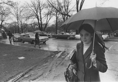 A female student walks to class in the rain; This photo is in the 1969 Kentuckian on page 105, image number 1