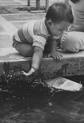 Boy plays with toy boat in the fountain