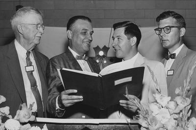 T. R. Bryant (left) and H. F. Massey (right) stand with two men holding a book; Lexington Herald - Leader staff photo