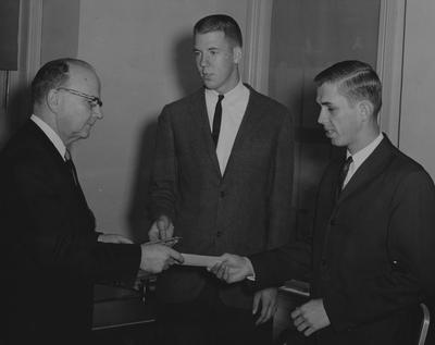 Two students receiving checks from an official