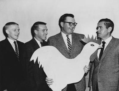 Members of the University of Kentucky poultry judging team assure their coach, Thomas H. Johnson (right) assistant poultry husbandman, that this wooden rooster which serves as a bulletin board for the University of Kentucky Poultry Club members is in no way connected with the storybook character; From left to right: Jack Otis, Ashland; William Conder, Harrodsburg; Thomas J. Campbell, Nicholasville; and Johnson