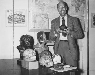 Dr. Charles Snow, physical anthropologist, with model skulls, busts, and artifacts