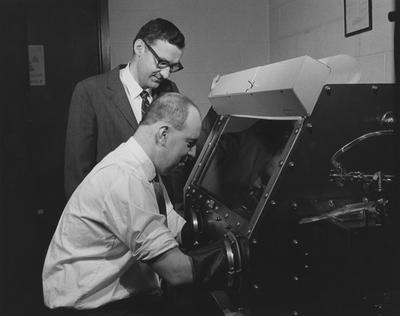 Dr. William Ehmann, University of Kentucky professor of Chemistry (standing), and his research associate Dr. John Morgan conduct tests on lunar samples in a glove box containing dry nitrogen