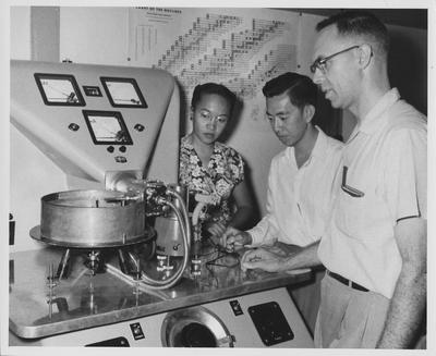 Clifford R. Keizer (right), professor of Chemistry, looks on as two graduate students operate one of the University of Indonesia's chemical laboratory x - ray machines; The students are Miss Mansdjoeriah (left) and Mr. Oei Djiong Gie; Professor Keizer was one of 16 American technicians working at the University of Indonesia's Technical and Science Faculties (colleges) in Bandung under an ICA financed contract with the University of Kentucky