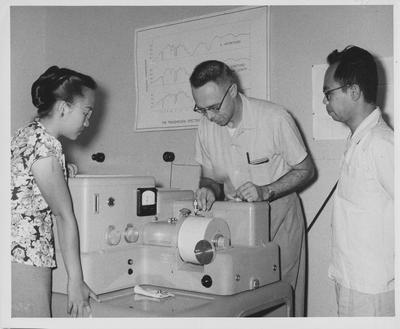 Clifford R. Keizer (center), professor of Chemistry, shows University of Indonesia graduate students, Miss Mandjoeriah and Isrijn Noerdin how to operate an infra - red spectrometer; The students are Miss Mansdjoeriah (left) and Mr. Oei Djiong Gie; Professor Keizer was one of 16 American technicians working at the University of Indonesia's Technical and Science Faculties (colleges) in Bandung under an ICA financed contract with the University of Kentucky