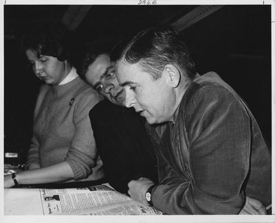 Michele (Mike) Fearing (left) and Norris Johnson (center), Thursday editors of the Kernel, listen to Professor Harry Ritter (right) as he tells them how to layout the sports section of the Kernel; This image is in the 1961 Kentuckian on page 296, image 3