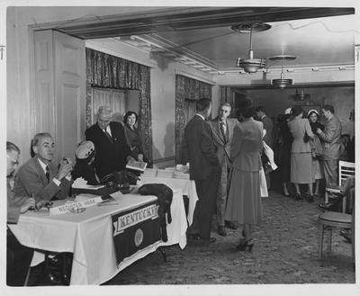University of Kentucky headquarters at the Kentucky Education Association in 1952 at the Brown Hotel? in Louisville; Dr. Hambleton Tapp at the registration table; Facing camera in central group is Dr. Harold Adams