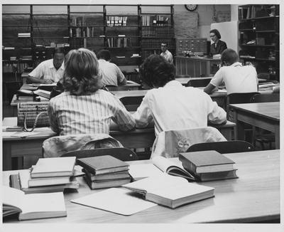Education students studying in the Education Library in the basement of Taylor Education; Emily Dawson, education librarian at desk on the right