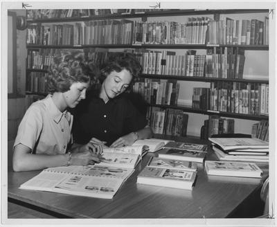 Two women students find materials for supplementing classroom textbooks in elementary and secondary education in the College of Education Library; This image is in the 1963 Kentuckian on page 272, image 1