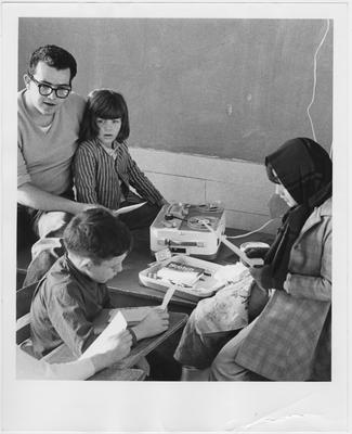 A man helps students read along as they listen; Photographer: Nancy Johnson