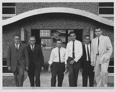 Men pose in front of a building