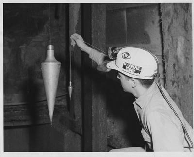 Dennis R. Keefer, a mining engineering student at the University of Kentucky, compares a 50 pound plumb bob with one of normal size