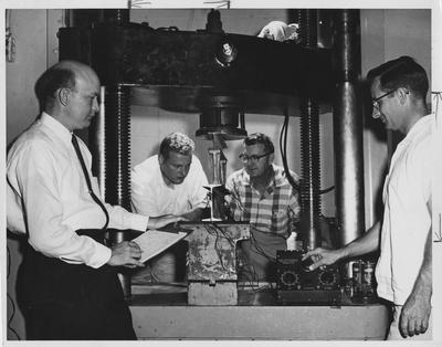 Men using a machine press; From left to right: Russell Puckett, Charles Schimpeler, Professor David Blythe, and John A. Dearinger