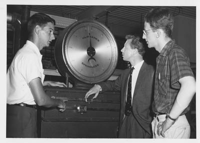 David Dingwall (center) and Adrian Napper (right), civil engineering students at the University of Durham, touring the College of Engineering; Showing them scales used in the hydraulics laboratory is Lewis N. Melton, Barbourville, civil engineering student at the University of Kentucky; Dingwall and Napper spent the Summer in Kentucky under to sponsorship of David Blyth, head of the University of Kentucky Department of Engineering