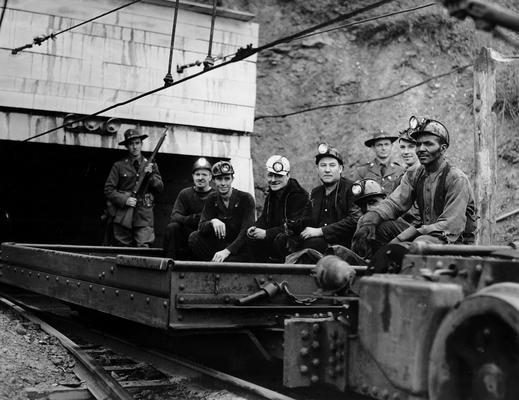 Miners leaving a mine entrance in a cart with police watching