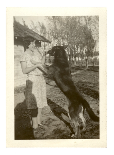 Irene, standing outside, playing with her dog.  Handwritten on verso, 