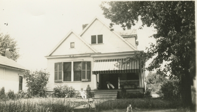 house with man on eh porch, child, tricycle, and dog in the yard