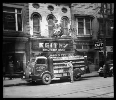 Kentucky Club Ginger Ale truck parked in front of stores on the                             side of East Main; John G. Epping Bottling Works; Thorpe's                             Tailoring Department, Keith's Bar and Chop House; Question Mark                             Cafe, 133 East Main Street