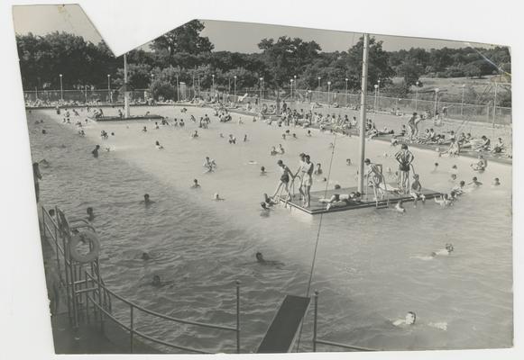 Swimming pool with two islands in the middle with people sitting and standing on them, people swimming in the water, amusement attraction, Joyland Park  - stamped on back of photograph MACK HUGHES PHOTOGRAPH 503 E. HIGH LEXINGTON, KY