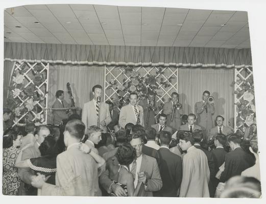 Two men singing on a stage with drums and trombones and cello being played behind them, people in the audience dancing, Joyland Park  - stamped on back of photograph MACK HUGHES PHOTOGRAPH 503 E. HIGH LEXINGTON, KY