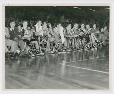 Basketball team on the bench: Frank Ramsey, Bill Spivey, Lou Tsioropoulis, Walt Hirsch, C.M. Newton, Bobby Watson, Shelby Linville, Adolph Rupp, Harry Lancaster