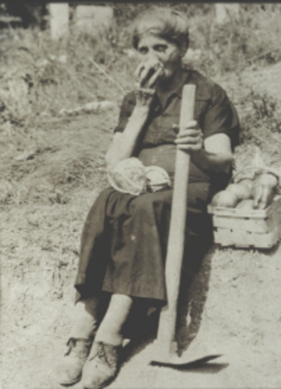 Elderly woman eating fruit on the side of a dirt road