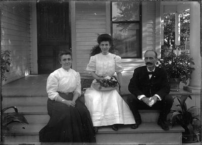 2 women and a man, possibly a family, sitting on porch steps