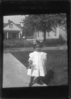 a young child (girl) standing on the front walk way holding a flower in her hand