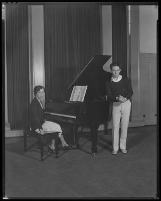 Girl seated at piano; man nearby