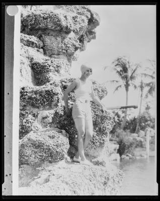 Young woman in swimsuit, standing on rocks above                             water
