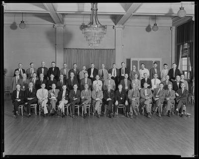 Men sitting in chairs, posed in ballroom