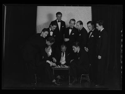 Men in tuxedos looking at a knife stuck in the table