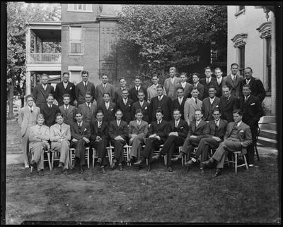 Young men seated, standing beside building