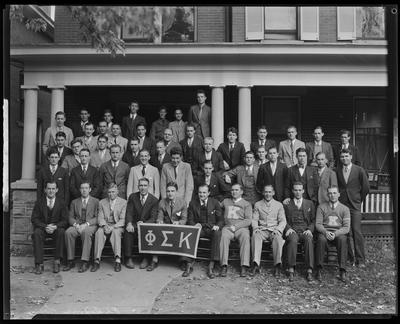 49 standing in front of a building, holding frat banner (Phi                             Sigma Kappa)