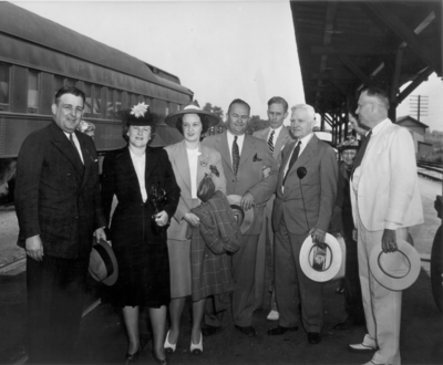 Group of five men and two women at a train station standing in front of a train (Point Orient)