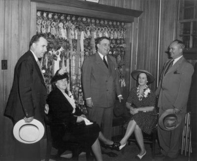 Three men and two women conversing in front of a cabinet filled with prize ribbons and badges