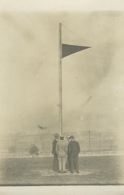 flag with 4 unidentified man gathered around the flag pole circa 1910