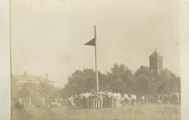 group of men protecting the 1913 flag by linking arms and standing around the flag pole circa 1910