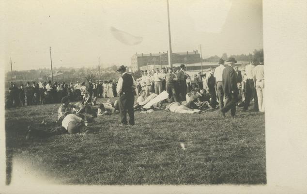 a group of unidentified men are guarding the flag pole, while other smaller groups are wrestling on the ground, people watching from sidelines circa 1910