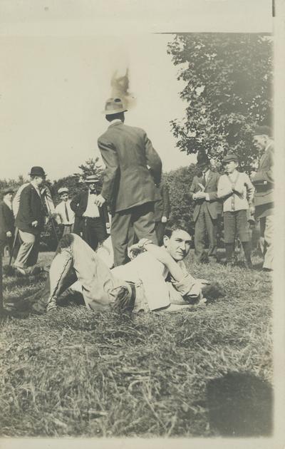 2 unidentified men wrestling on the ground, other unidentified people are standing around some are watching circa 1910