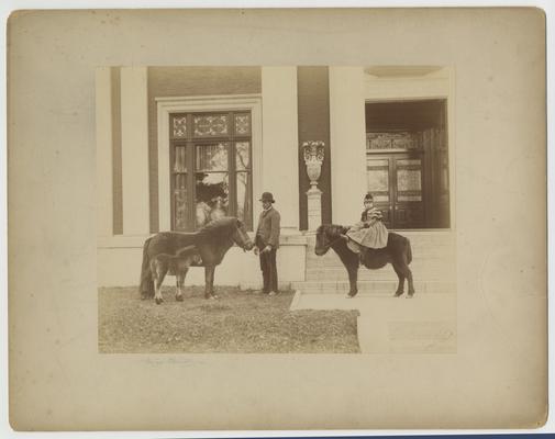 Clara D. Bell riding a Shetland pony, Booky with an unidentified man, a pony and foal in front of Bell Place