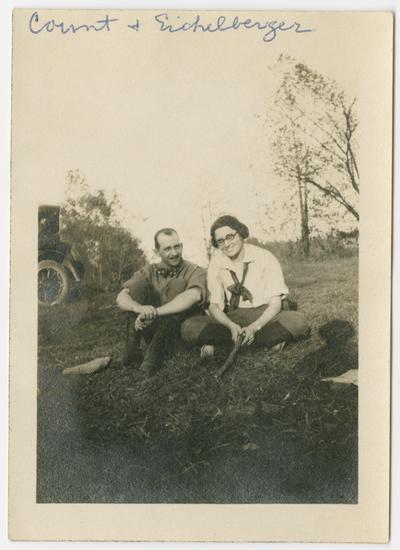 Count and Eichelberger, sitting cross-legged on the ground.  The edge of an automobile and trees are in the background
